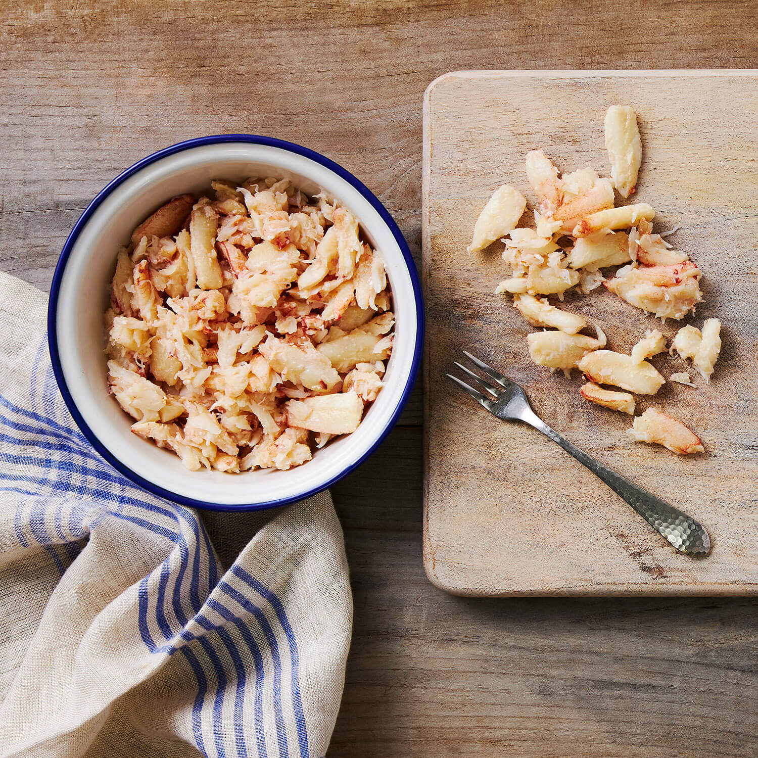 A bowl of Crab Meat on a wooden table with a cutting board and fork.
