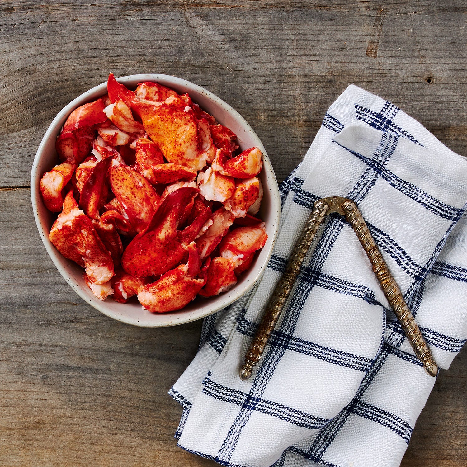 This photo shows a bowl full of Maine lobster Meat alongside a blue and white patterned dish towel resting under a set of shell crackers