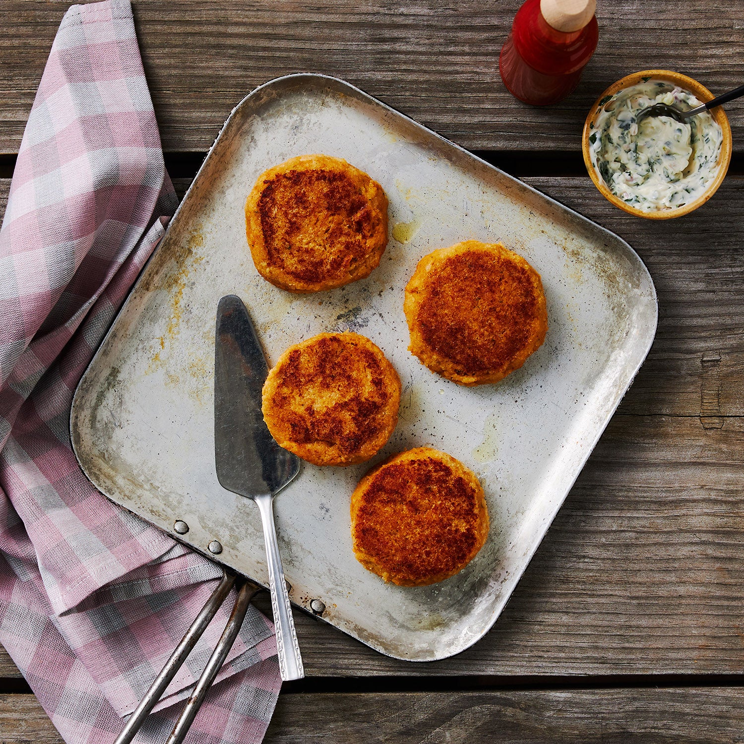 This photo shows 4 Crab cakes prepared perfectly on a square metal tray alongside a herb aioli dip