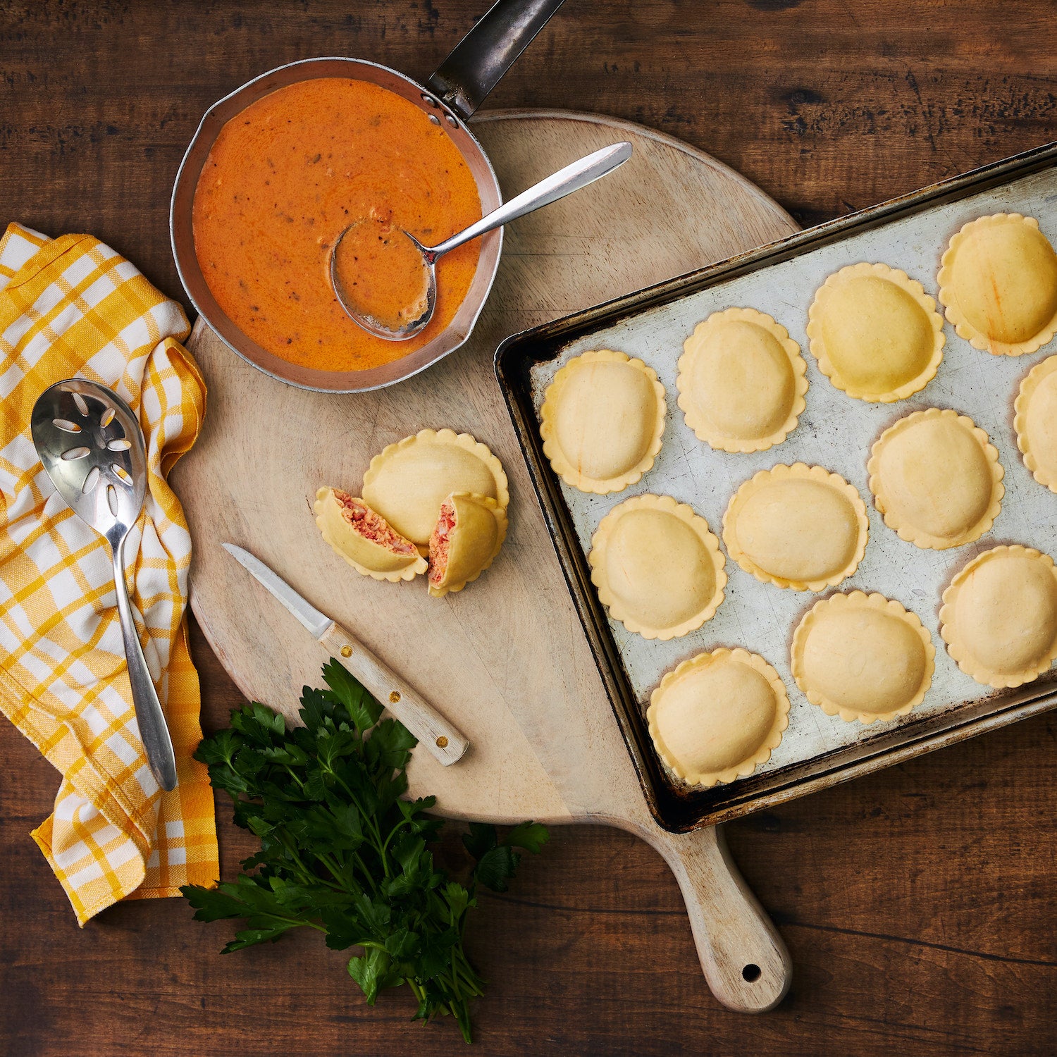 This image shows the Maine Lobster Ravioli laid out on a baking sheet placed onto a Wooden cutting board with a single ravioli cut in half revealing the mouthwatering filling that is inside.