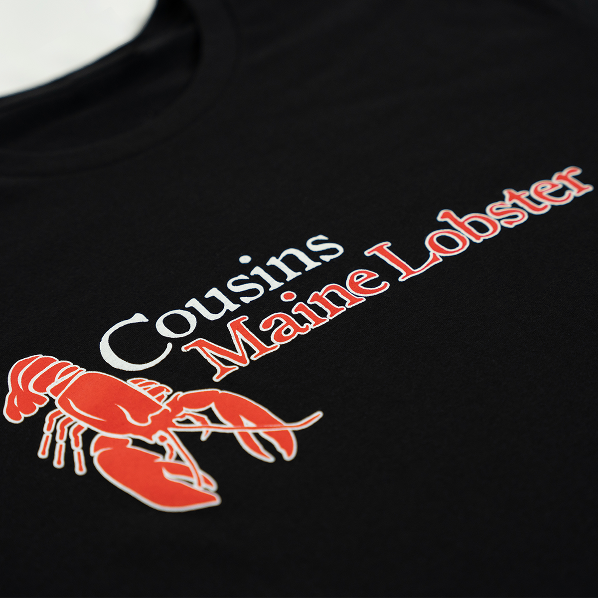 Black shirt with Cousins Maine Lobster logo featuring a red lobster illustration.