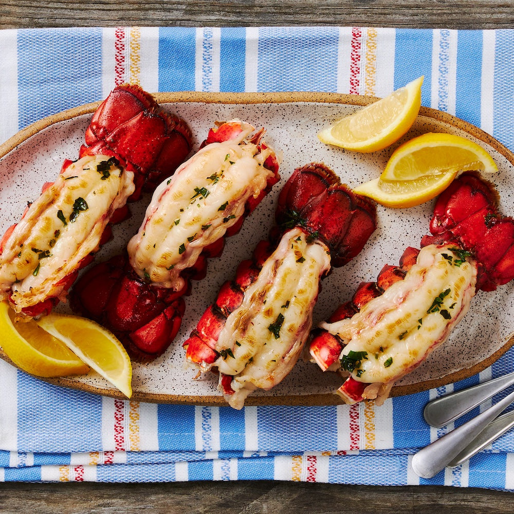 This image displays 4 Lobster Tails, Butterflied and cooked, On a plate with lemon wedges 