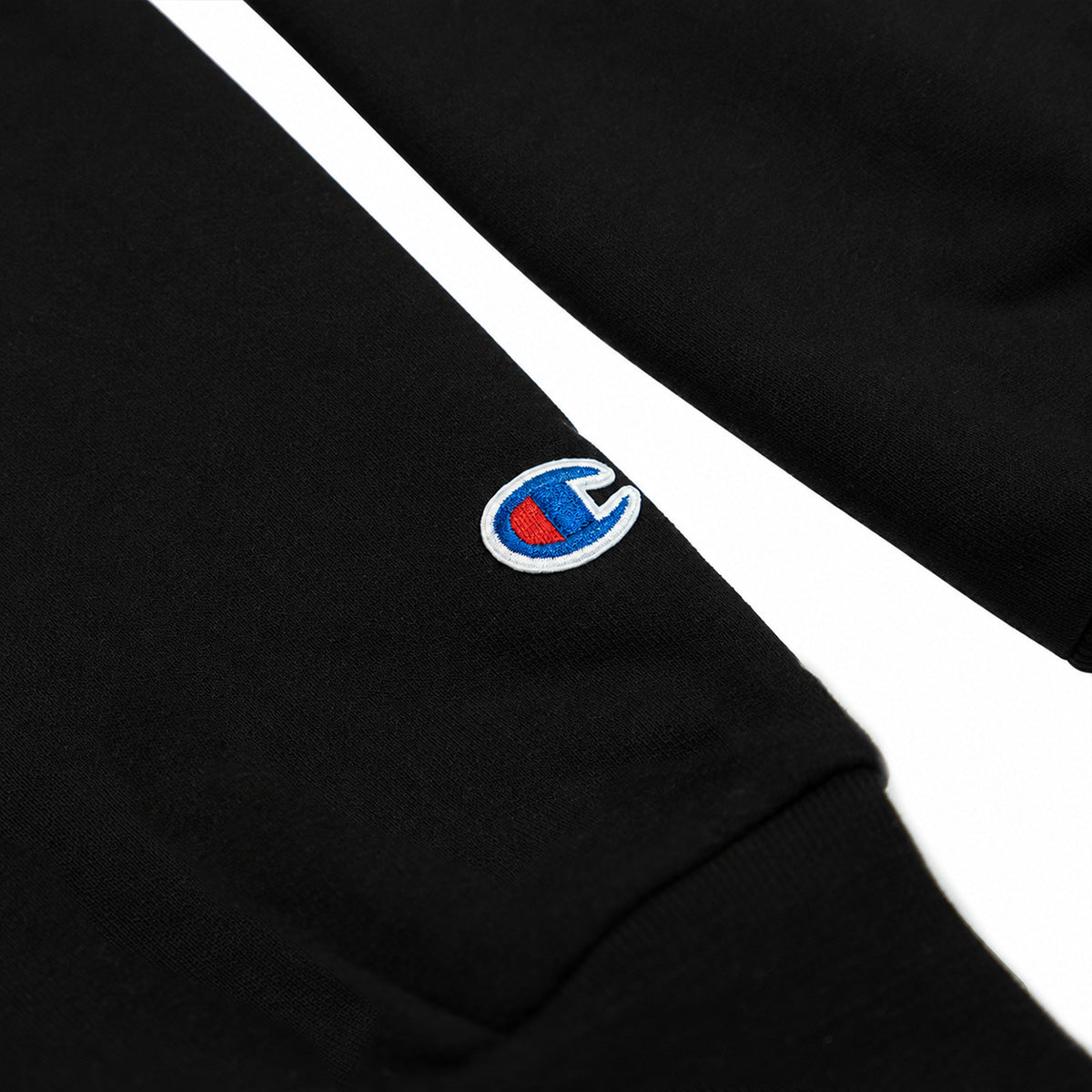 Close-up of black Champion crewneck sleeve cuff with embroidered red and blue Champion C logo