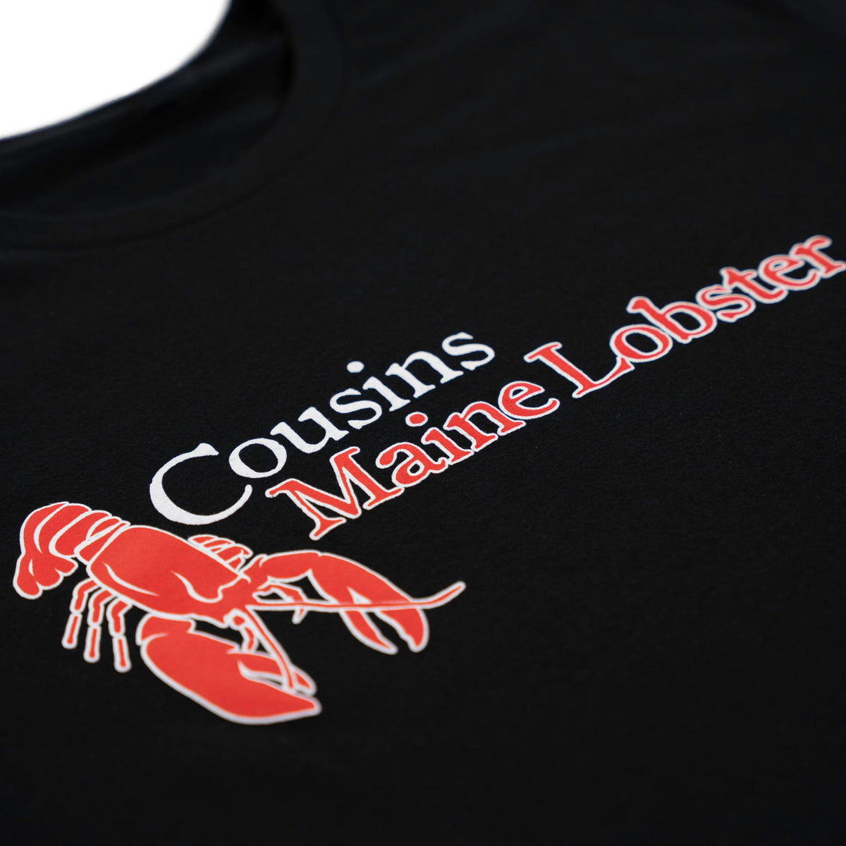 Black tee with Cousins Maine Lobster script logo in white and red and a red lobster graphic