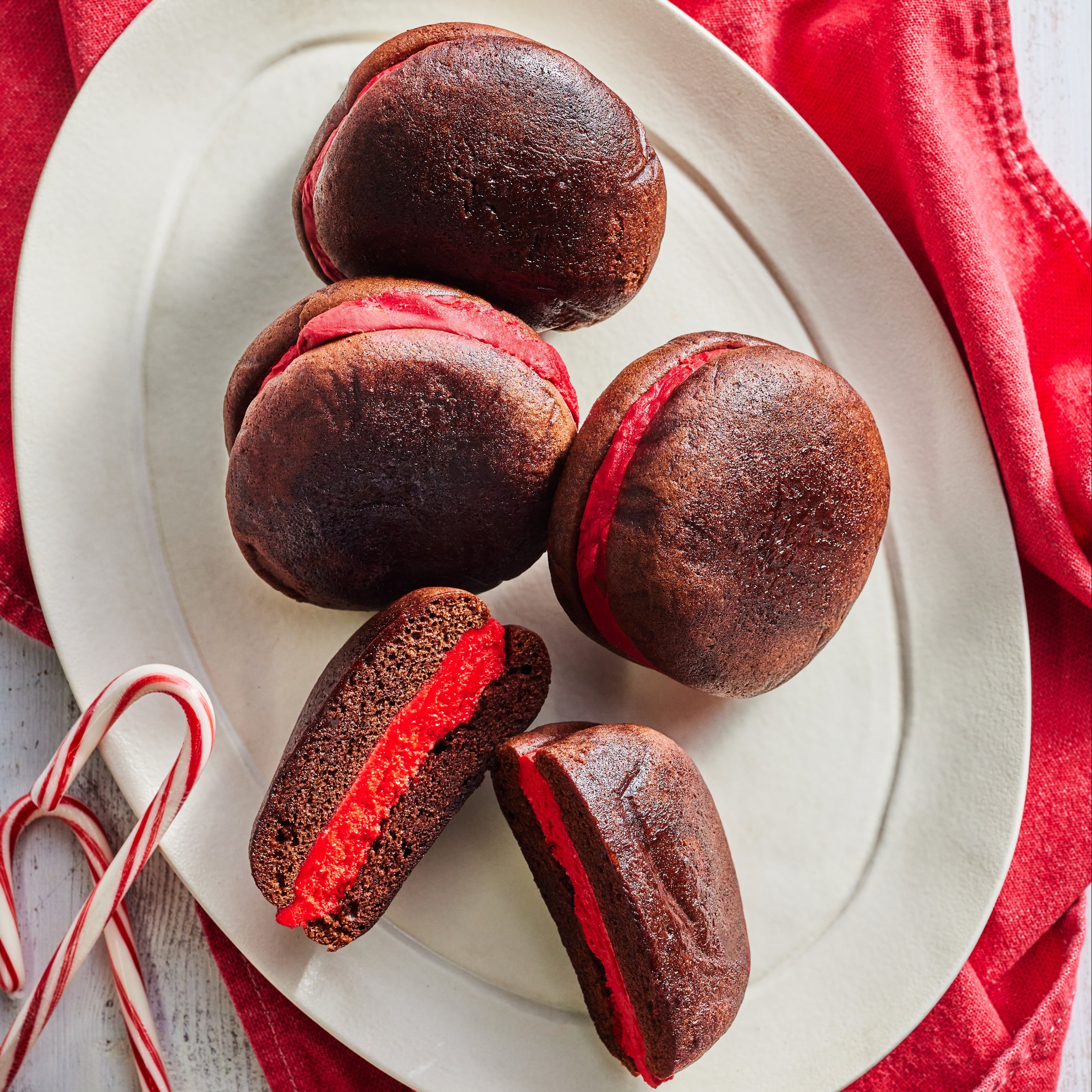 Four Chocolate Peppermint Whoopie pies plated alongside a red linen and 2 candy canes