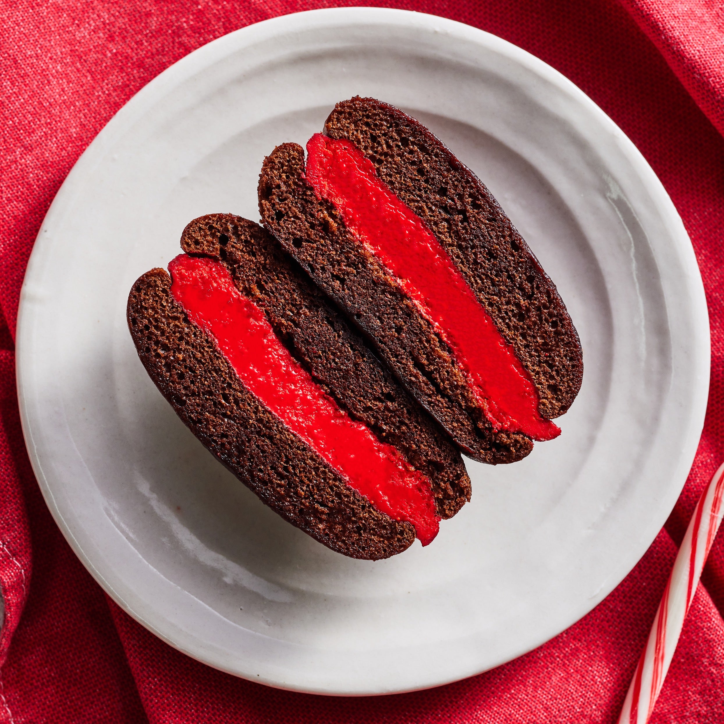 A single Chocolate Peppermint whoopie pie, cut in half showing the cross section, plated alongside a red linen