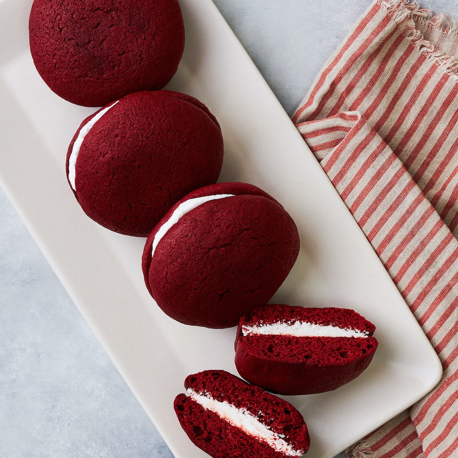 This photo shows the 4 pack of Red velvet whoopie pies with one cut in half showing a cross section of the moist cake and creamy filling 