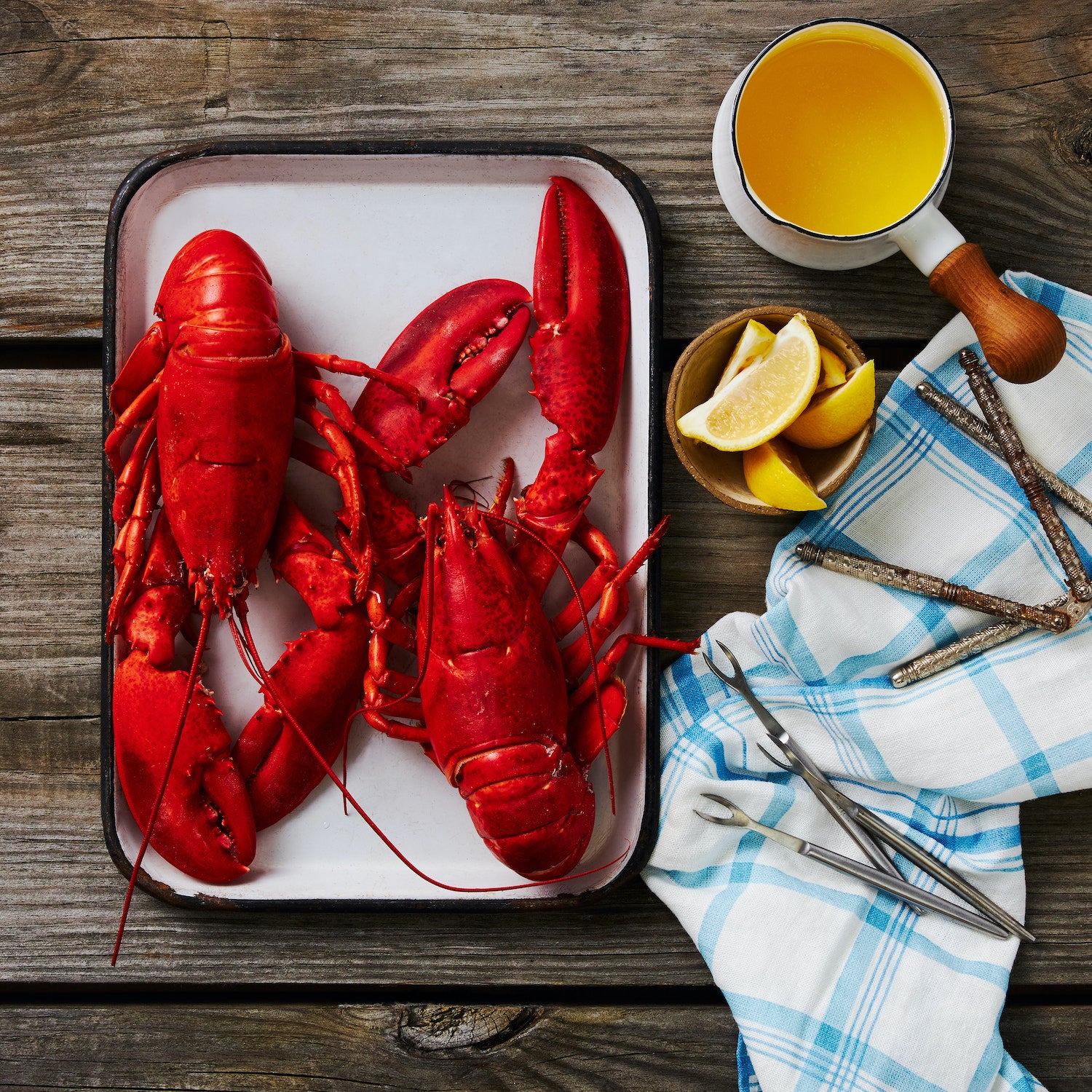 This photograph shows the two lobsters on a tray freshly steamed alongside a small pot of melted butter, Lemon wedges, claw crackers and picks to remove all of the delicious Maine lobster meat