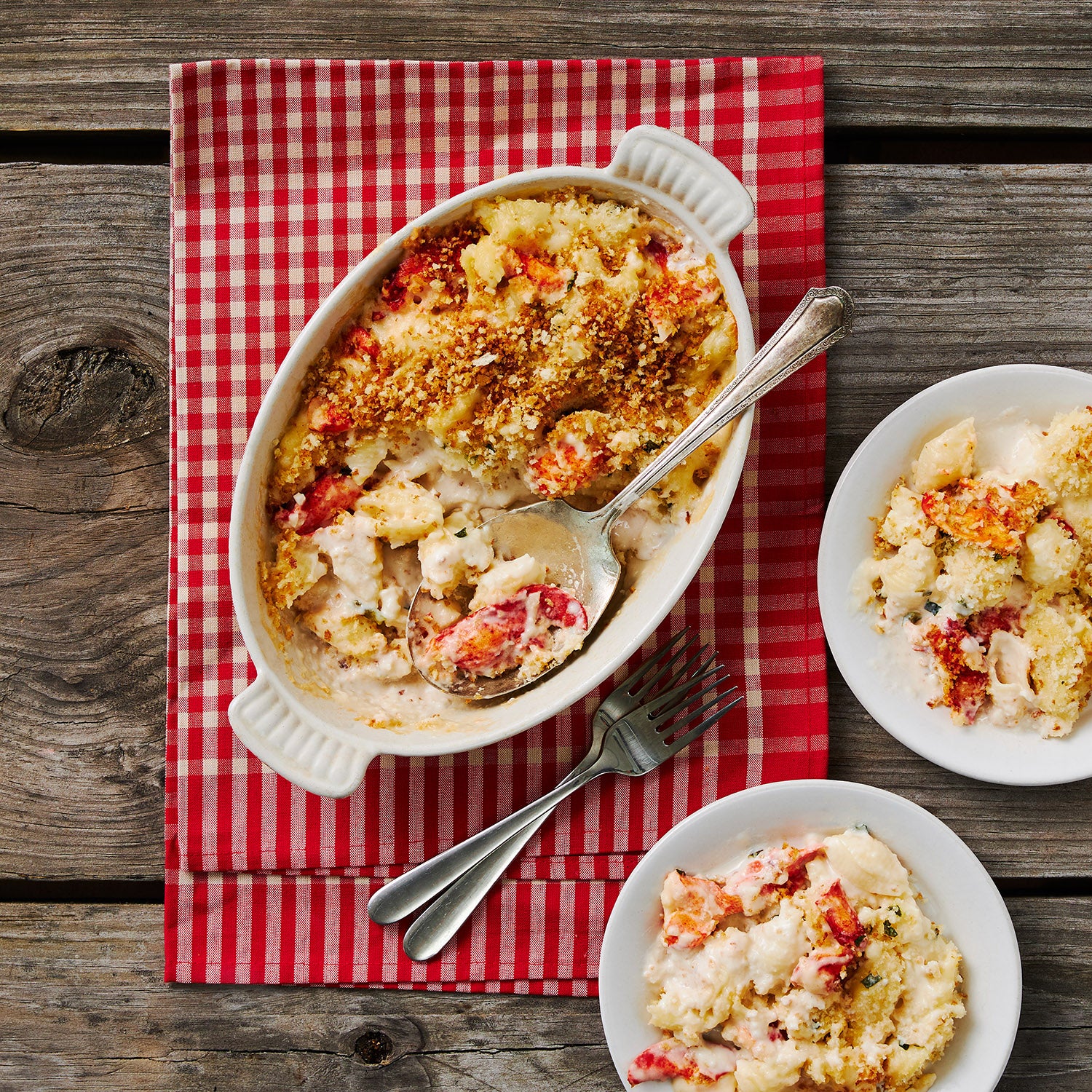 This photograph Maine Lobster Mac and cheese fresh out of the oven topped with beautifully browned bread crumbs and beside the baking dish there are two dishes with mouthwatering servings of mac and cheese ready to be devoured