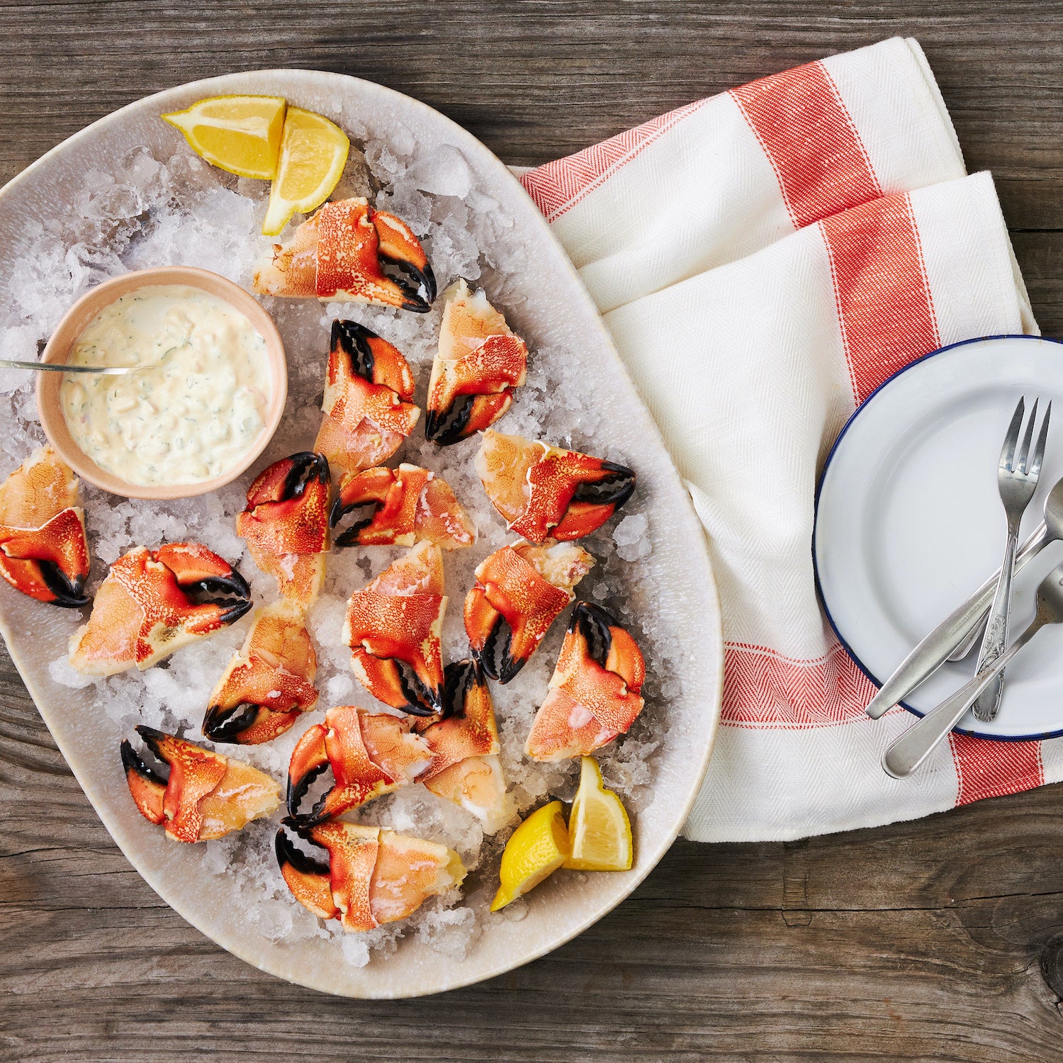  This image shows over a dozen crab claws resting on a tray of chipped ice alongside lemon wedges and a creamy sauce to enjoy together.